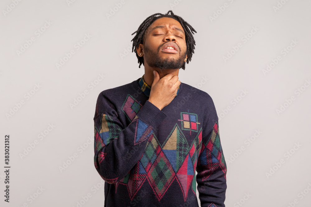 Depressed african man with beard touching neck feeling discomfort while swallowing, sore throat, tonsillitis. Indoor studio shot isolated on gray background Depressed african man with beard touching neck feeling discomfort while swallowing, sore throat, tonsillitis. Indoor studio shot isolated on gray background