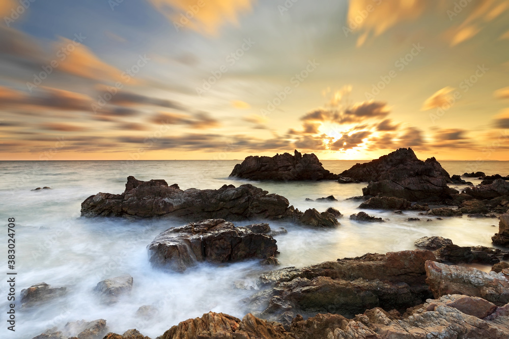 Obraz premium Long exposure of sea wave impact the stone with clouds moving on beach in the sunset time, Eastern of Thailand