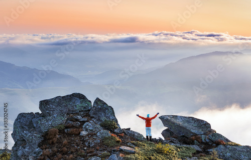 Successful sporty girl is standing at the edge of the precipice. Mountains landscape in the foggy morning. Sunrise. Autumn.