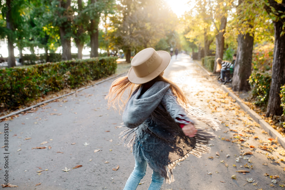 Freedom of movement. Little girl 7 years old in a warm cape and hat is dancing on the alley of the park at sunset in autumn
