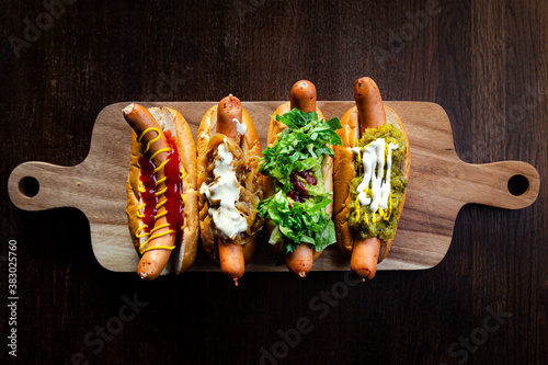 фотографія Four types of delicious hot dogs on a wooden board and brown table top view