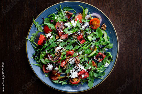 Watermelon and ricotta salad with walnuts, rocket, cherry tomatoes, cucumber and balsamic vinaigrette on a blue plate top view photo