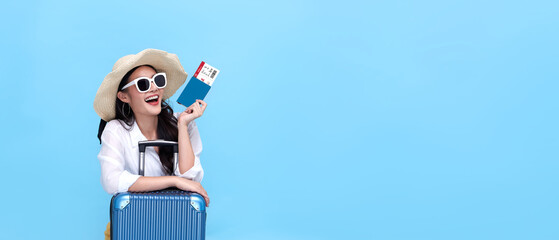 Happy young Asian tourist woman holding passport and boarding pass with baggage going to travel on holidays on blue background.