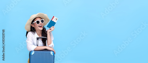 Happy young Asian tourist woman holding passport and boarding pass with baggage going to travel on holidays on blue background.
