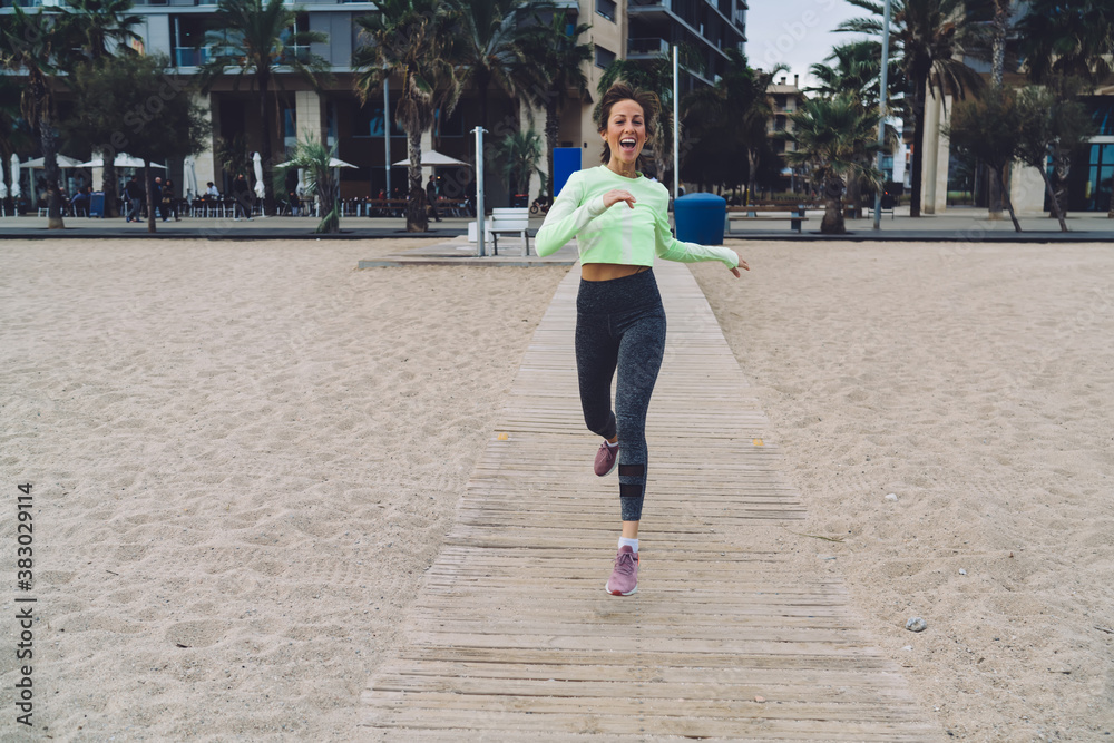 Portrait of excited fit girl running to beach seashore satisfied with wellbeing healthy lifestyle, Joyful Caucasian woman in trendy tracksuit laughing at camera during morning cardio training