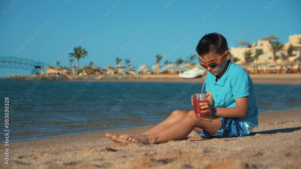 Attractive teen boy in sunglasses drinking lemonade at beach. Boy putting glass Attractive teen boy in sunglasses drinking lemonade at beach. Boy putting glass