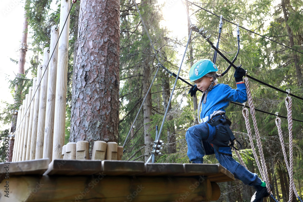 Kid overcoming hanging ropes obstacle in forest