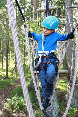 Kid overcoming hanging ropes obstacle in adventure park