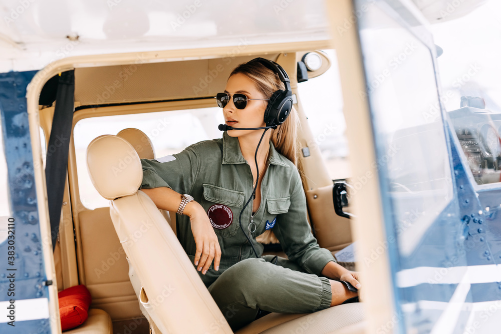 Woman pilot in private airplane cockpit, wearing headset and sunglasses. - obrazy, fototapety, plakaty 