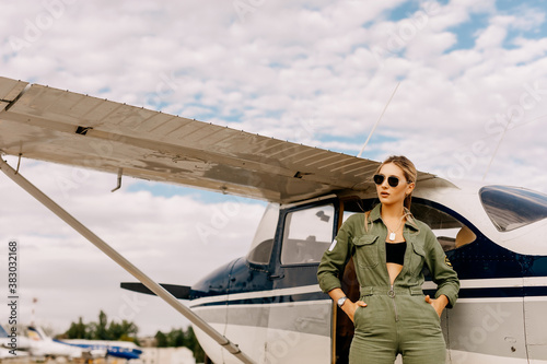 Woman pilot wearing overall and sunglasses, standing next to a private plane.