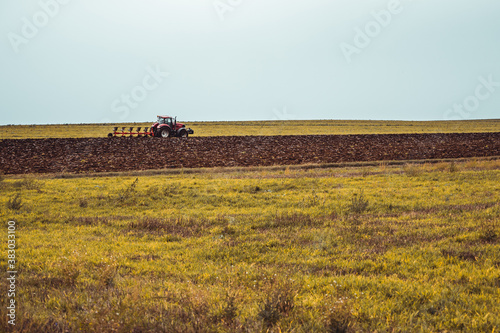Tractor plowing the fields in the countryside. Agricultural tractor plowing the field. Red Tractor with plow.