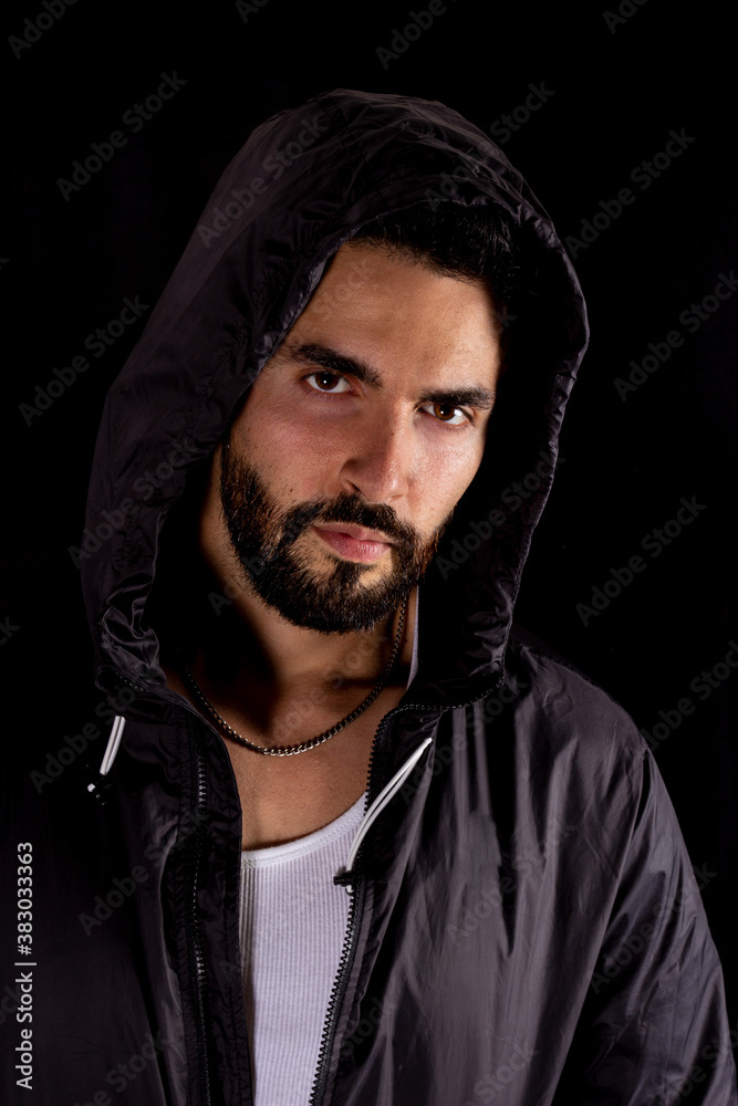 Dramatic medium shot of handsome bearded man wearing dark hood on a black background