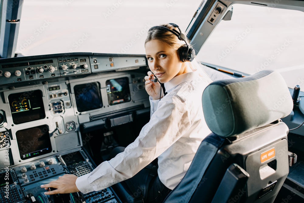 Woman pilot sitting in aircraft cockpit, wearing headset, looking at camera. - obrazy, fototapety, plakaty 