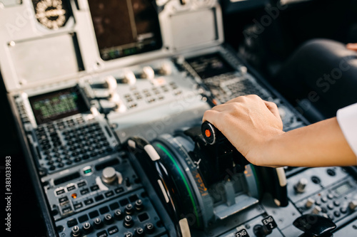 Pilot hand on airplane engine control board in cockpit.