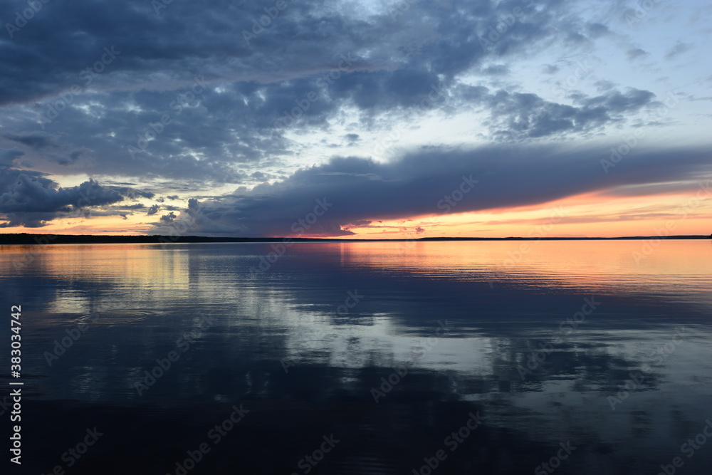 Sunlight in the dark clouds of the twilight sky is reflected in the calming water of the lake