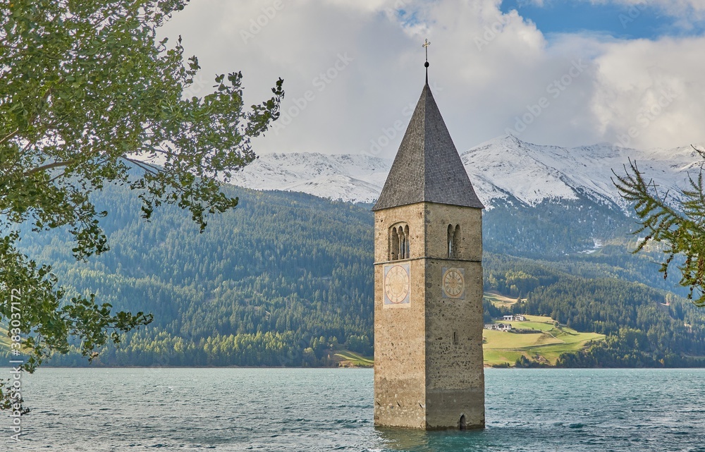 Submerged church tower in the lake reschen in tirol. Lago di Resia with snow covered mountains in the background.