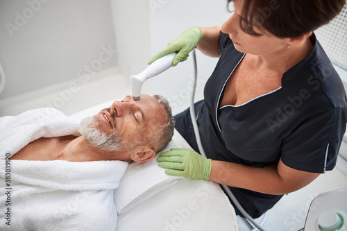 Skillful beautician helping revive skin of an elderly man