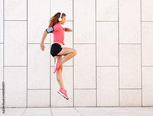 Dynamic sporty woman with headphones jumping near wall.