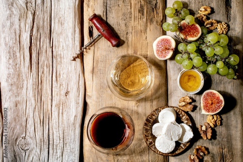 Glasses of red and white wine with grapes, figs, goat cheese and walnuts over old wooden background. Flat lay, copy space