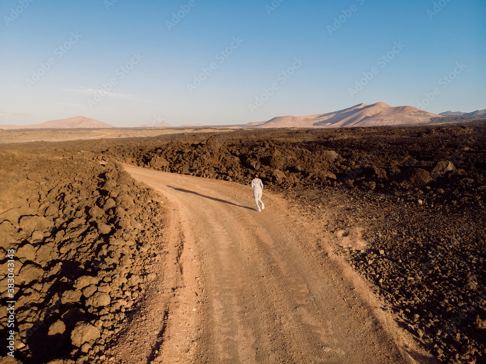 Aerial view with sporty woman run on dirty road amid lava field. Lanzarote, Canary Islands.