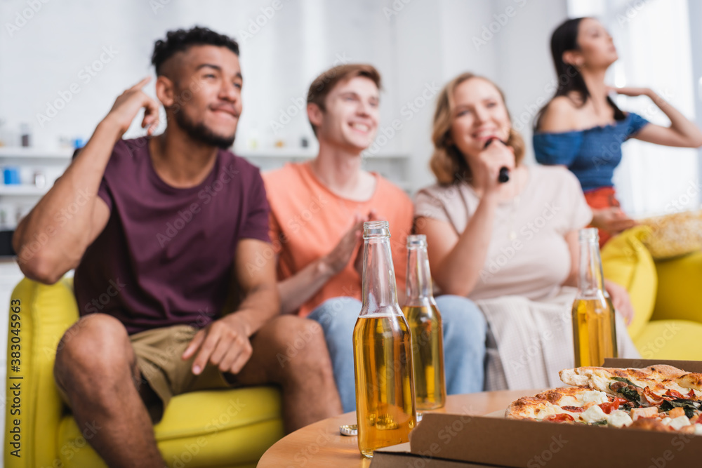 selective focus of multiethnic friends singing karaoke near beer and pizza selective focus of multiethnic friends singing karaoke near beer and pizza