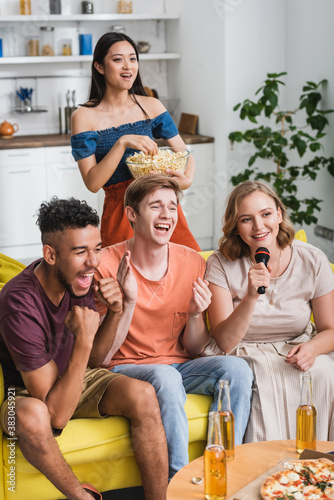 excited multiethnic friends applauding while singing karaoke during party