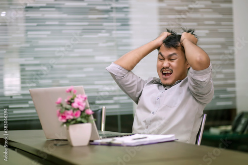 Asian business people are feeling stressed about the job with laptop and paper on the wooden table in the office. Asian men are worried when their work is unsuccessful.