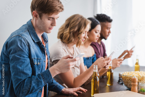 selective focus of multiethnic friends messaging on smartphones near beer during party