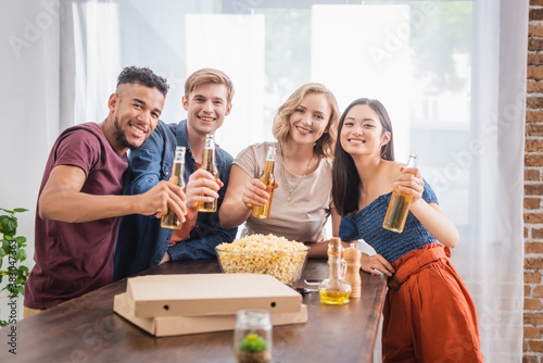 joyful multiethnic friends looking at camera while holding bottles of beer