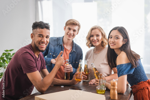 excited african american man showing thumb up near multicultural friends during party