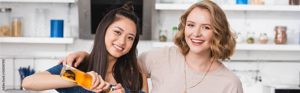 panoramic shot of joyful asian woman opening bottles of beer near friends during party