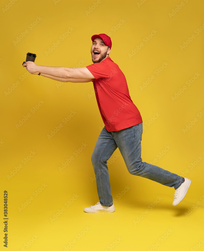 Delivery man in red cap blank t-shirt uniform isolated on yellow background. Guy employee hold takeaway cup of coffee Delivery man in red cap blank t-shirt uniform isolated on yellow background. Guy employee hold takeaway cup of coffee