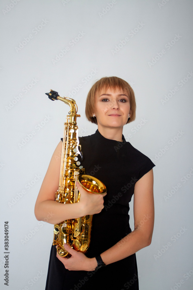 Fototapeta premium Portrait of Young woman with a gold saxophone. Woman holding a musical instrument