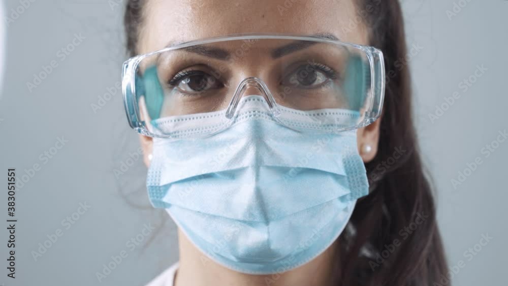 Stock video of a caucasian woman putting on a face mask. She is wearing protective glasses.