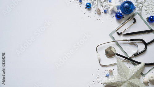 Christmas medical banner christmas decor white stars,blue balls, snowflakes, stethoscope and tablet on white background top view. Copyspace. Medicine new year flatly. Doctor writes down the text