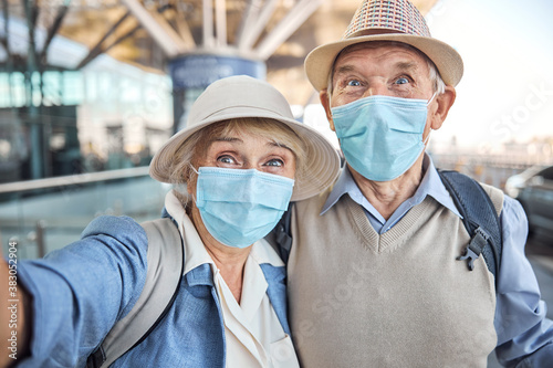 Two aged travelers in protective masks taking selfies