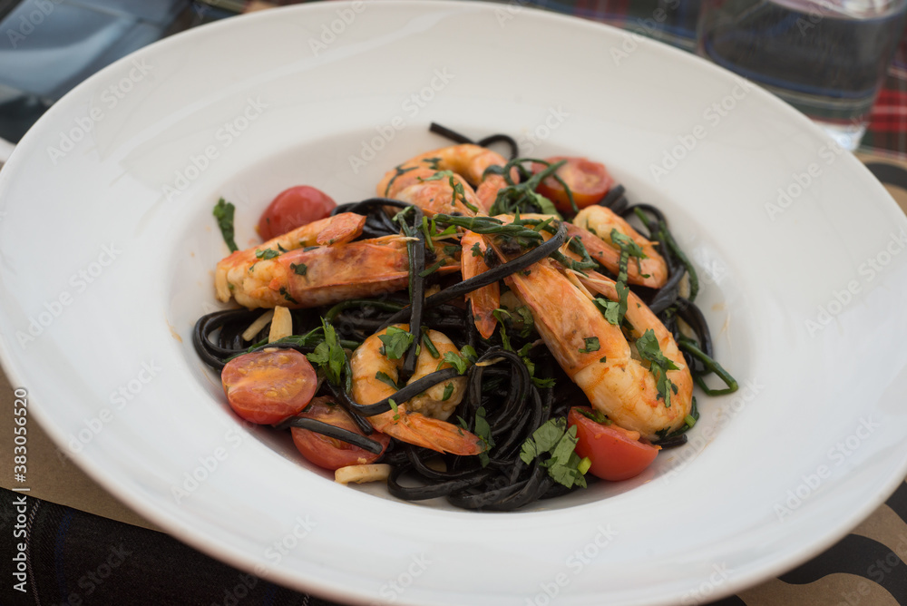 Closeup of shrimps , tomatoes and seaweed pasta in a white plate at the restaurant terrace in the street Closeup of shrimps , tomatoes and seaweed pasta in a white plate at the restaurant terrace in the street