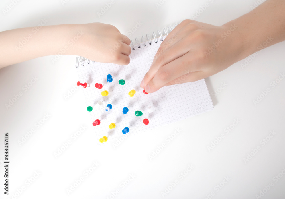 The hand of a child and a doctor sets multi-colored pins in a leaf on a white background. Autism development concept of a child thinking in games, autism, neurosonography The hand of a child and a doctor sets multi-colored pins in a leaf on a white background. Autism development concept of a child thinking in games, autism, neurosonography