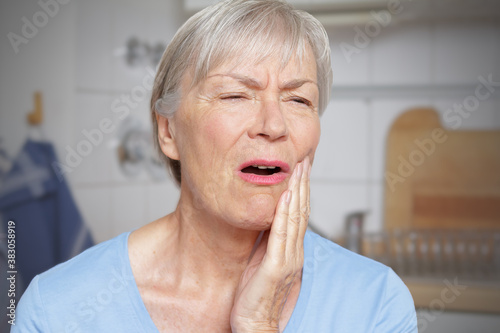 Acute toothache: elderly woman in her kitchen with a hand at her painful cheek. photo