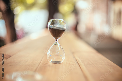 Hourglass on wooden table outdoors in the rays of sunlight