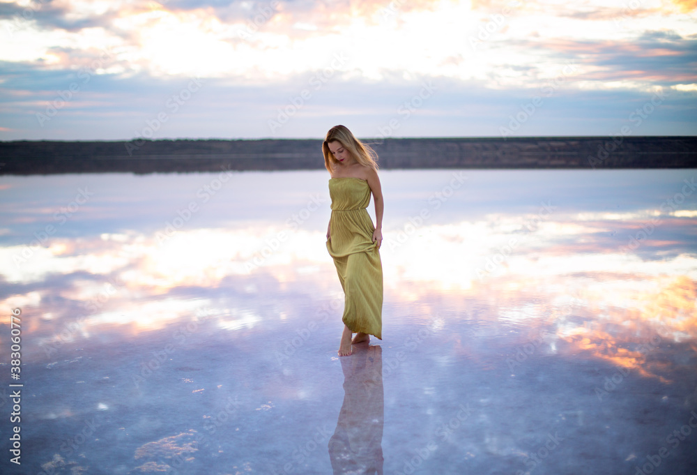 caucasian female with blonde hair in a light green dress on a pink color salty lake with still water against the backdrop of a beautiful pink sunset caucasian female with blonde hair in a light green dress on a pink color salty lake with still water against the backdrop of a beautiful pink sunset