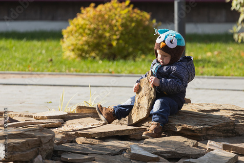Adorable little 1-2 year old toddler boy having fun and playing with stone on the playground, the child wears a blue jacket with an owl hat