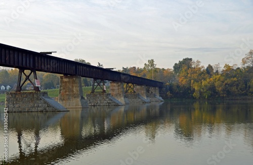 Autumn landscape with a railroad bridge and colourful  foliage reflecting in the water,  along the Grand River near Caledonia Ontario Canada © skyf