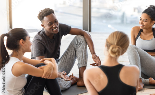 Multiethnic people sitting on mats relaxing after yoga training in modern studio