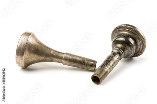 Two vintage trombone mouthpieces laying down on a white surface.  Close up of brass instrument mouthpiece with patina and wear.  Musical instrument accessories up close. photo