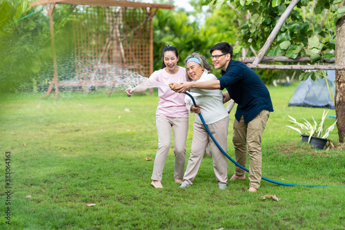Asian family happy smiling and watering green cultivated plants with a garden hose at home. Happy family concept. 4 people father Mather sun daughter.