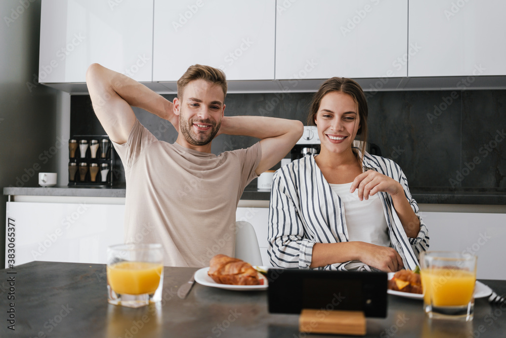 Young couple looking at cellphone while having breakfast at home