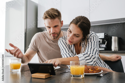 Young couple looking at cellphone while having breakfast at home