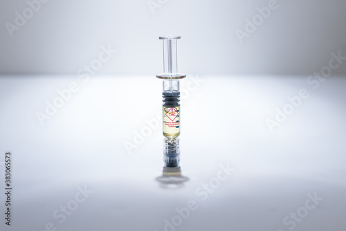 A syringe of marijuana distillate for refillable vaporizer cartridges.  On white surface with white background, spot light, with gradients.  Close up isolated shot.