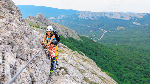 Young mother, child in safety equipment climb to mount top by via ferrata beginner route. Family travel adventure, hiking activity. Kids exploring nature on summer vacation. Weekend day walking tour photo